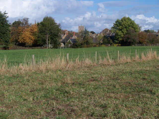 A rural landscape with a field, trees, and a church in the background.
