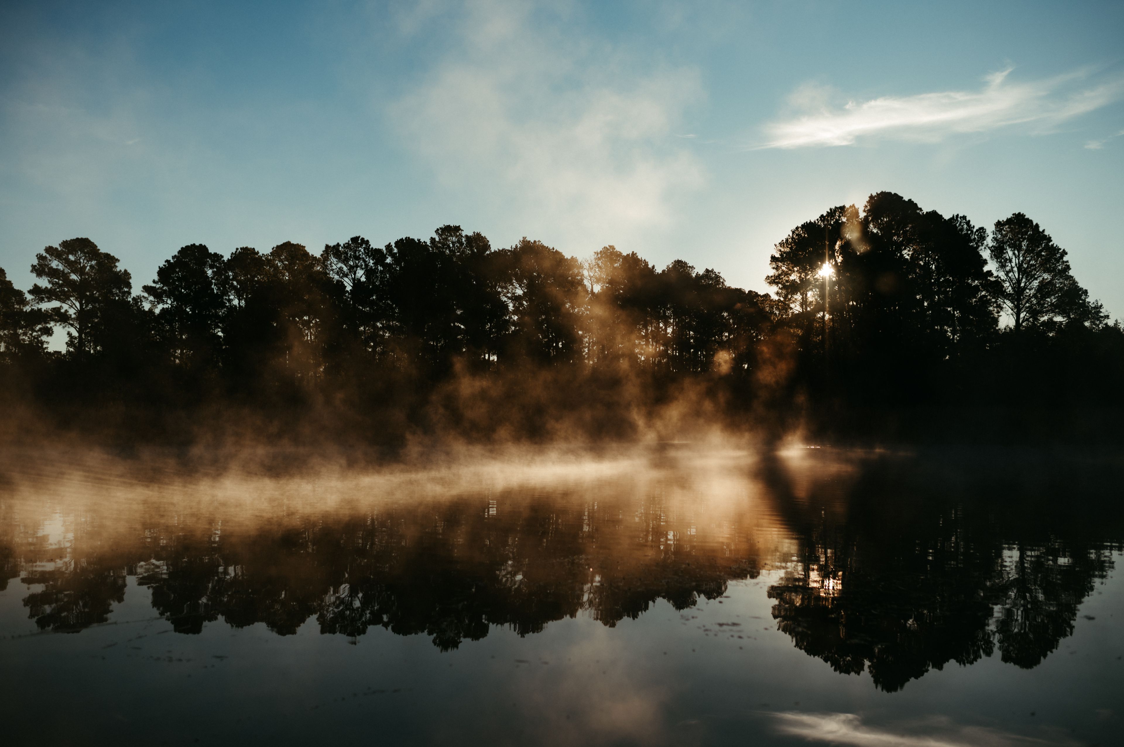 En stilla sjö med träd som speglar himlen och solljuset.
