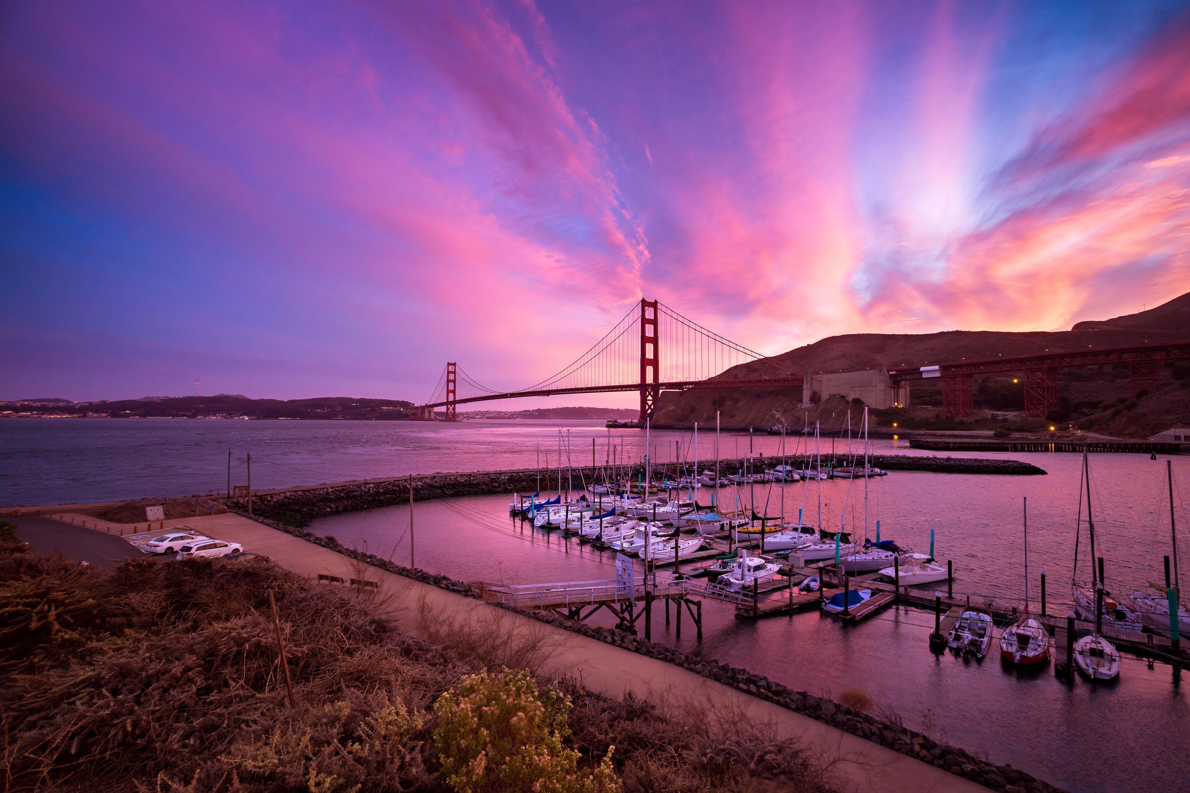 The Golden Gate Bridge at sunset with boats docked in a marina.