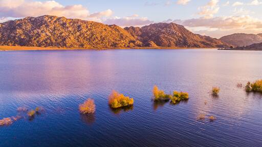 A calm lake with small islands and mountains in the background.