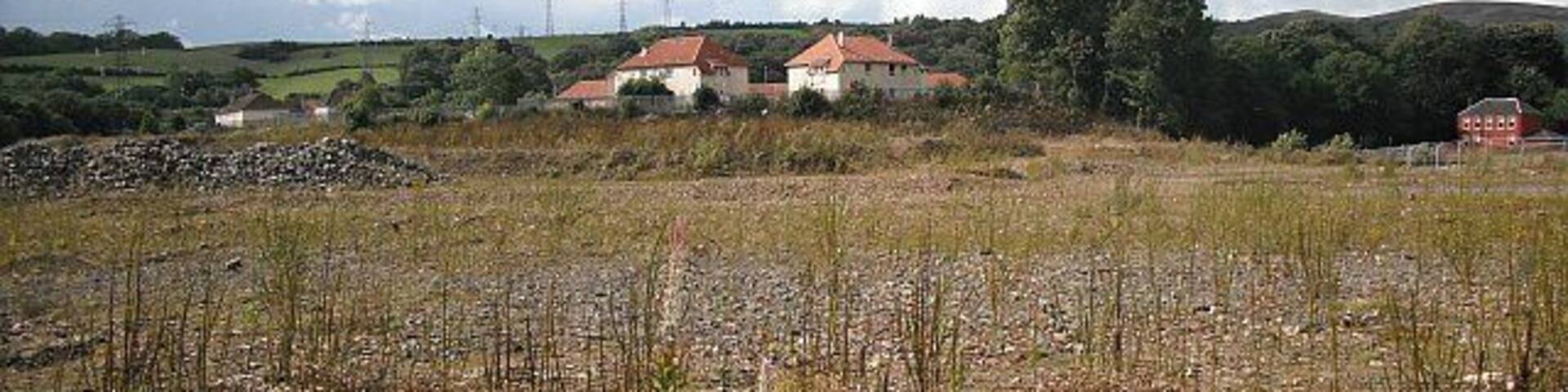 A rural landscape with a field in the foreground and houses in the background.