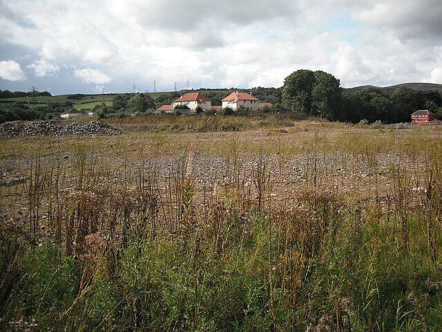 A rural landscape with a field in the foreground and houses in the background.