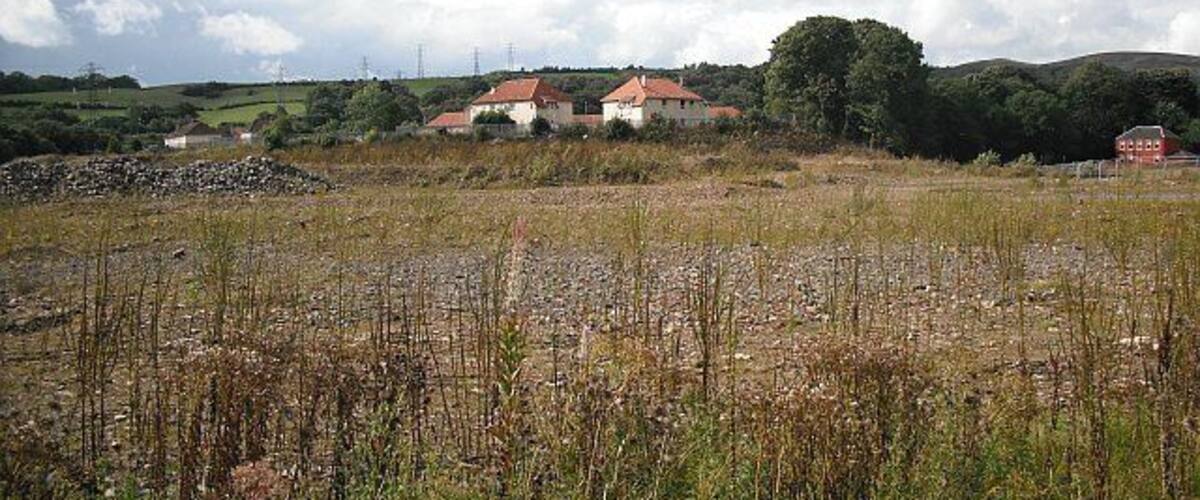 A rural landscape with a field in the foreground and houses in the background.