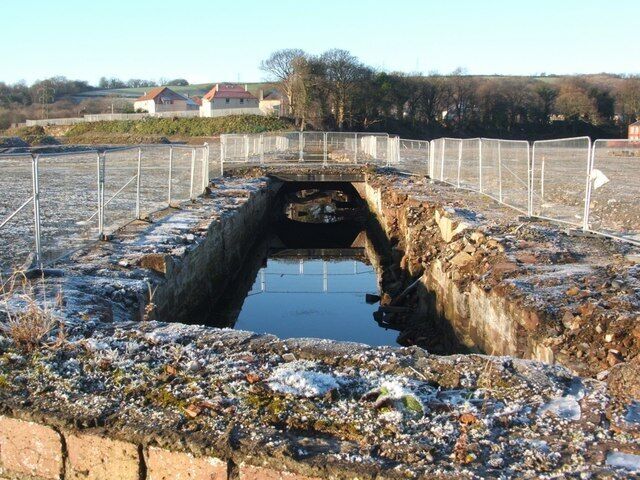 The Lade at Dalquhurn (exposed culvert). While the first half of the Lade (as reckoned from its intake), has long been exposed (1068180), this outflowing half has long been covered by buildings. At the time that this photograph was taken, the part of the Lade shown here had temporarily been exposed as a result of demolition work in Dalquhurn; it will presumably soon be covered again by subsequent construction work at that site. The houses in the background are in the Tontine area of Renton.