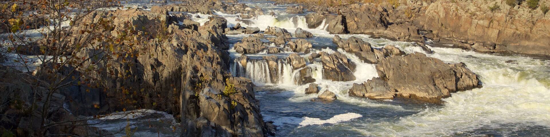 A river with a waterfall, surrounded by rocky terrain and autumn-colored trees.