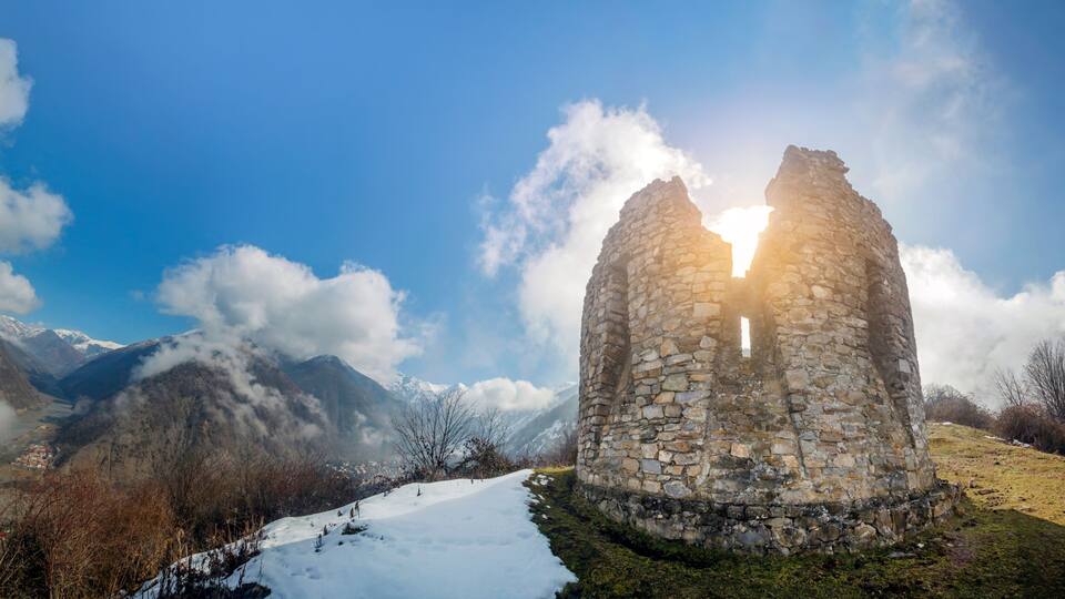 A stone ruin with a clear sky and snow-covered mountains in the background.