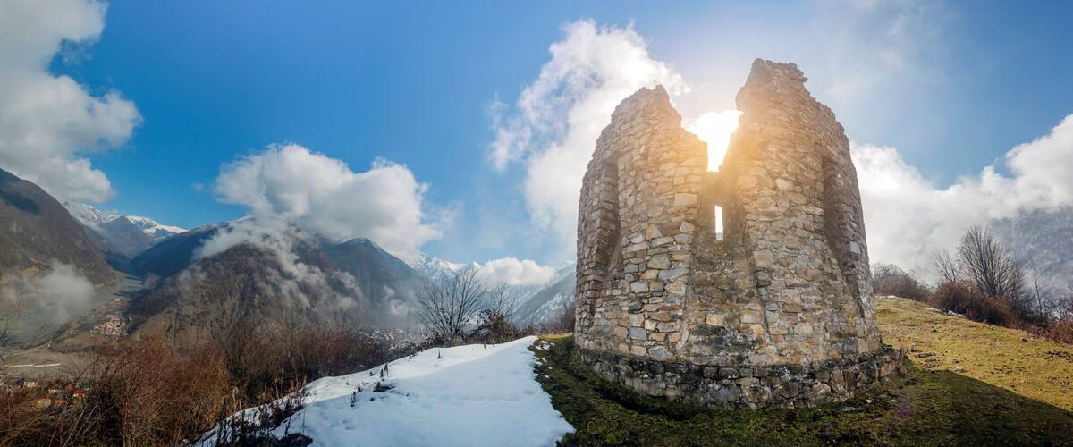 A stone ruin with a clear sky and snow-covered mountains in the background.