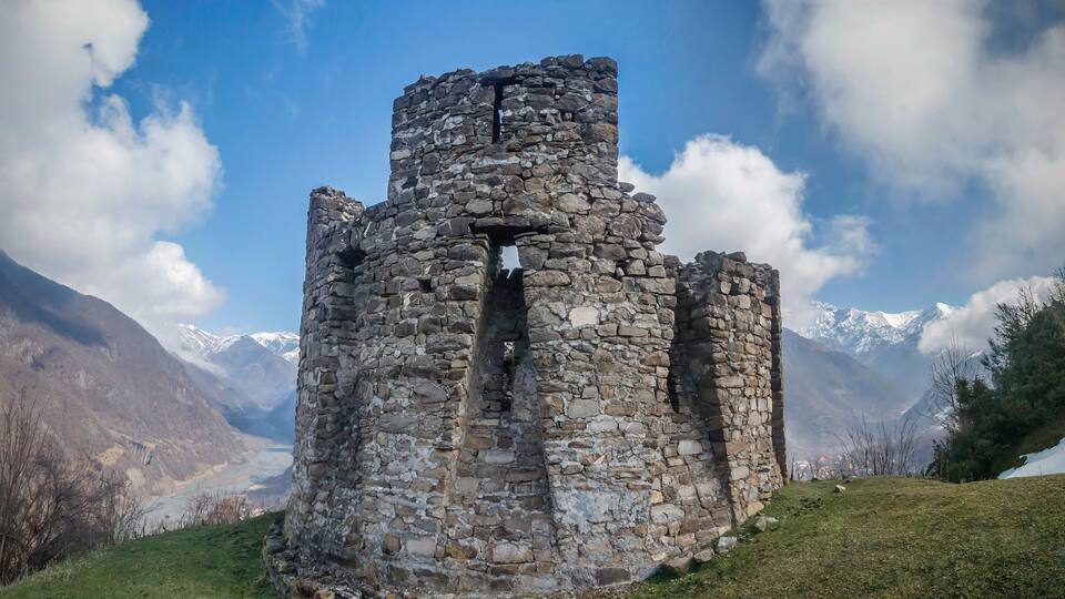 A stone tower with a narrow passageway, surrounded by mountains and a clear sky.