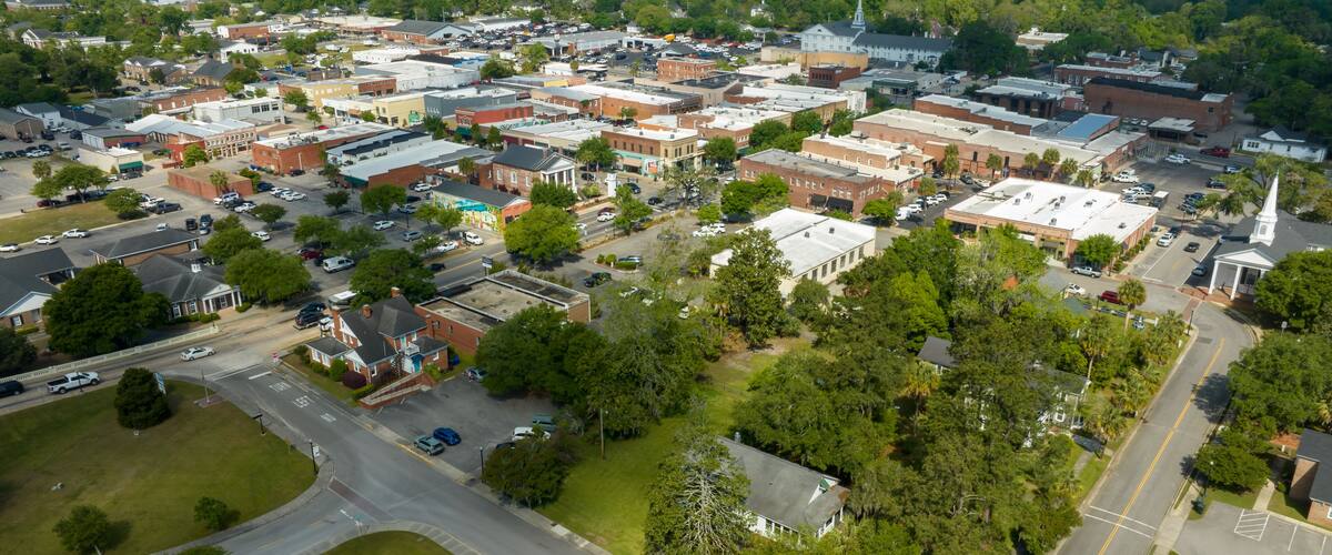 An aerial view of a town with a mix of commercial and residential buildings, a church steeple, and a large green park area.