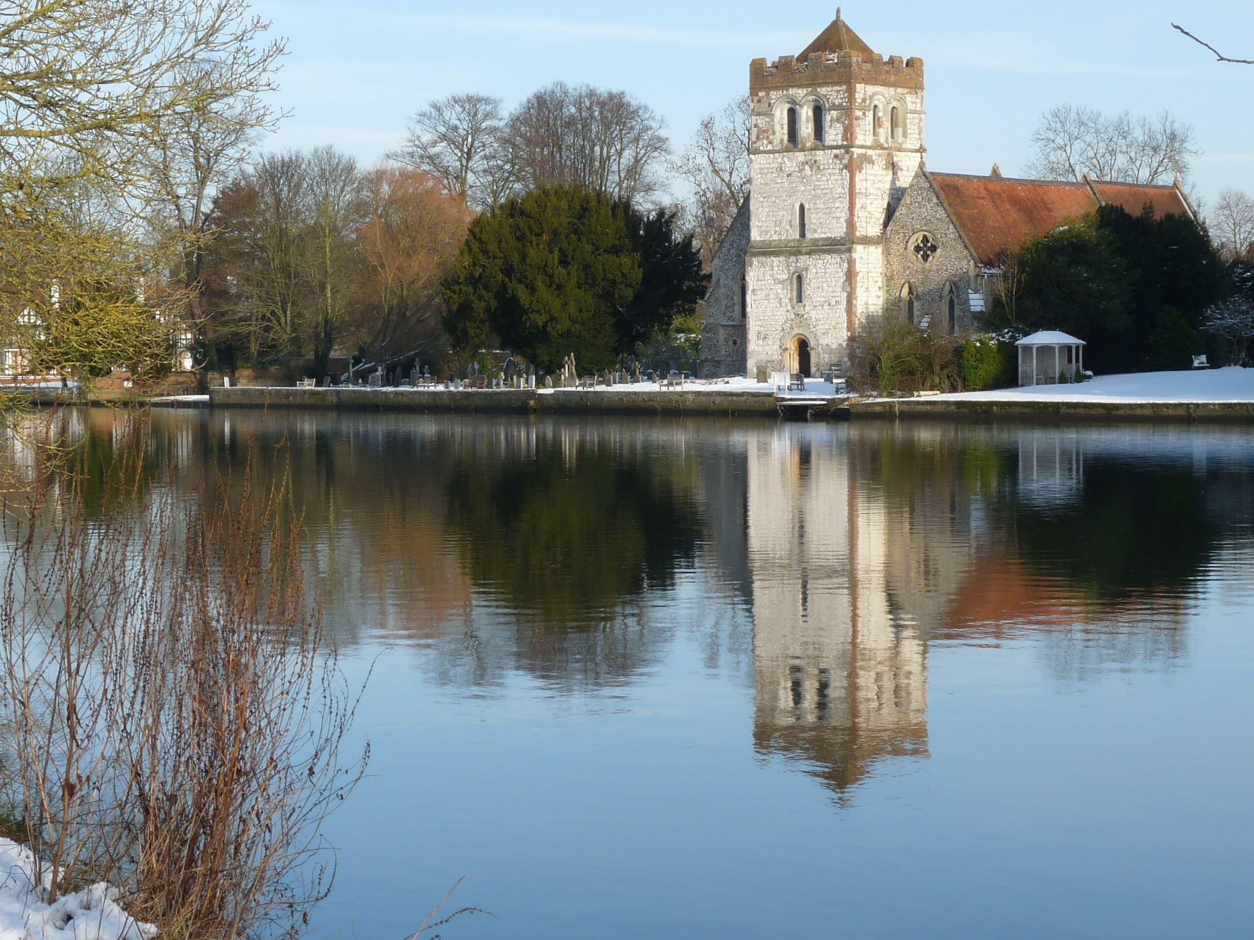 A historic stone tower by a calm lake, surrounded by trees and a gazebo.