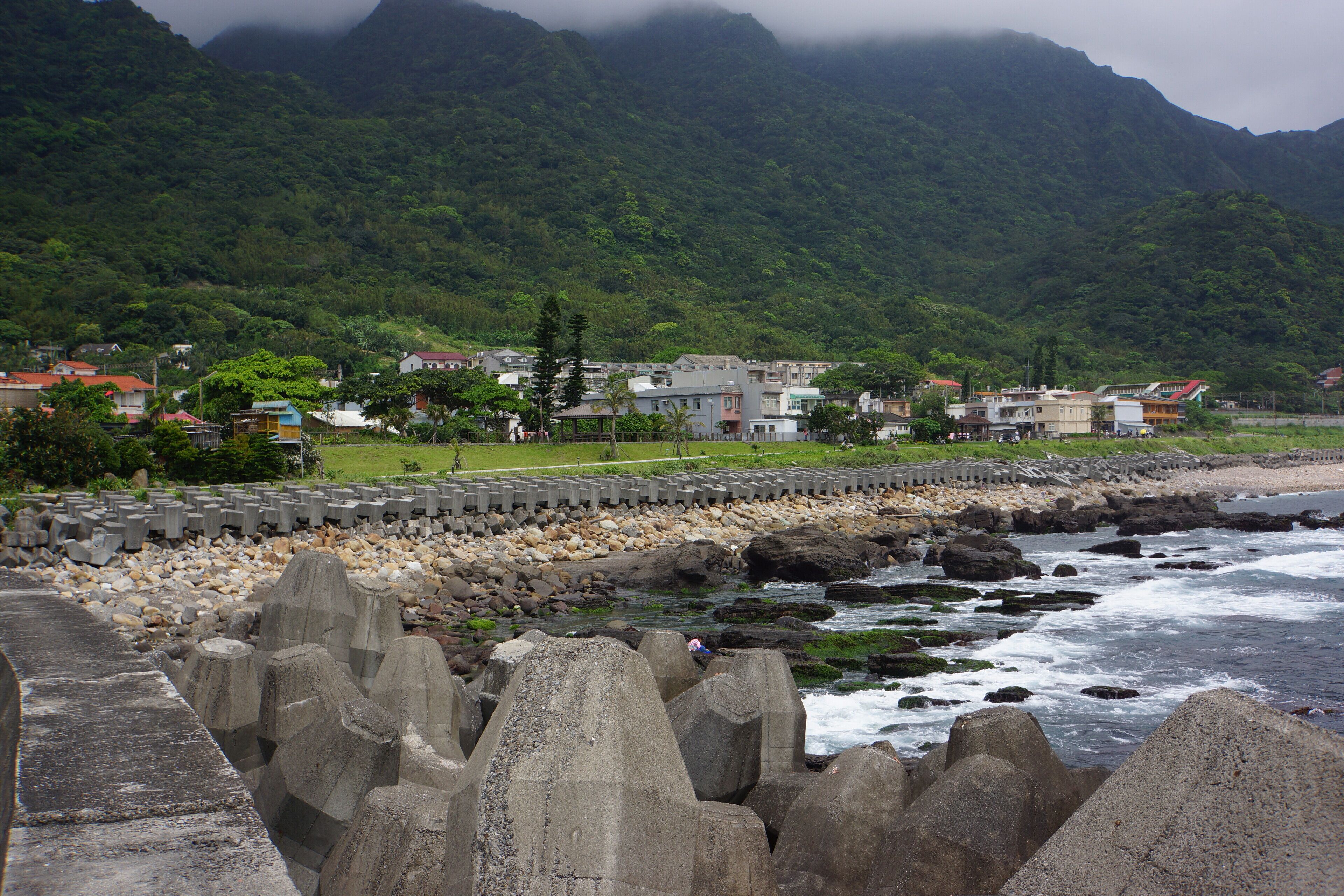 A coastal town with a rocky shoreline, houses, and a mountain in the background.