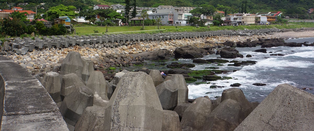 A coastal town with a rocky shoreline, houses, and a mountain in the background.