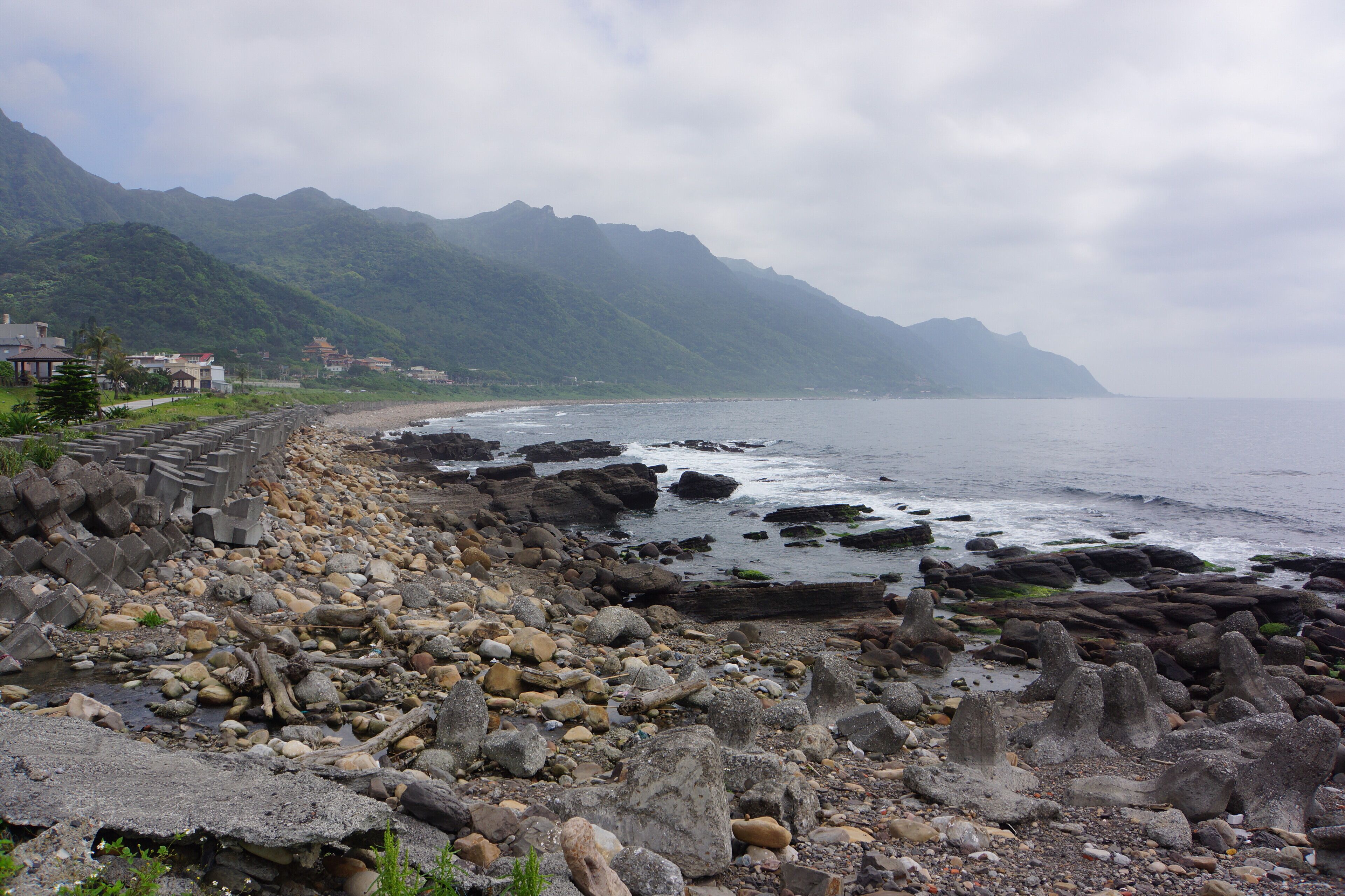 A rocky shoreline with a mountain backdrop and houses along the coast.