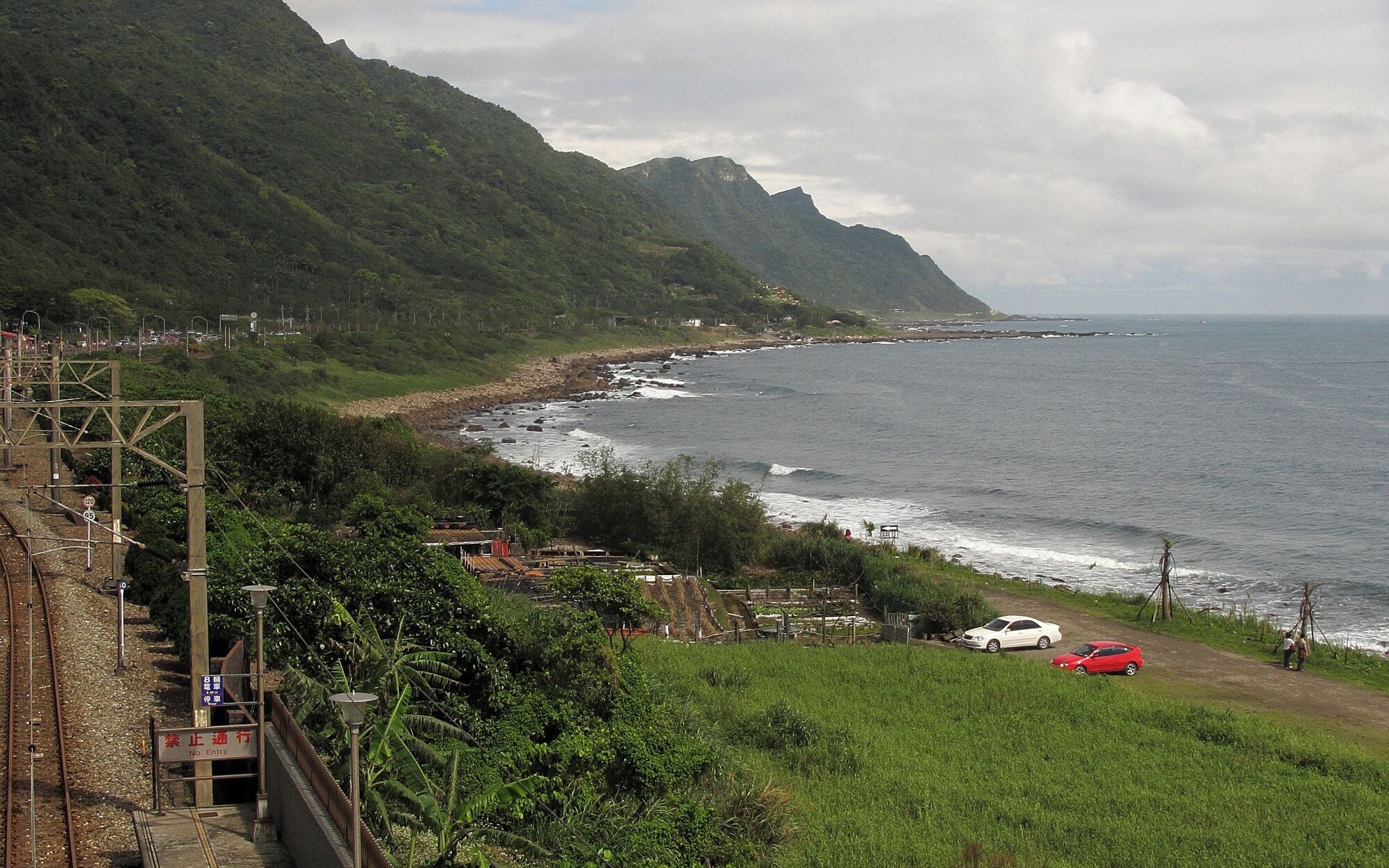 A coastal landscape with a railway track, a beach, and a mountainous backdrop.