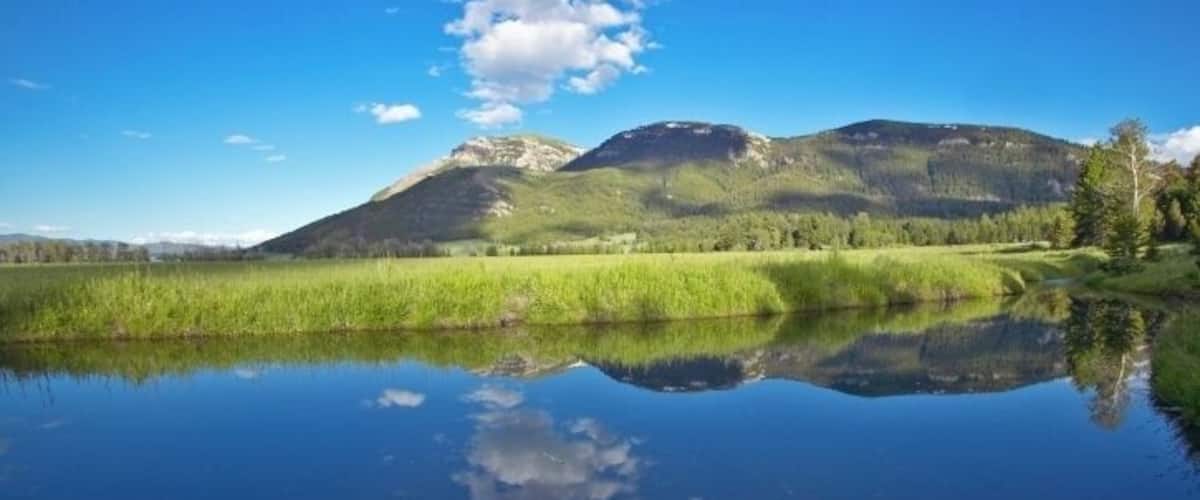 A calm lake reflecting a mountain range and clear blue sky.