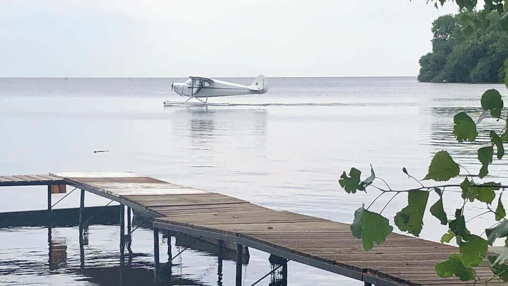 A seaplane on water, a wooden dock, and a forested island in the background.