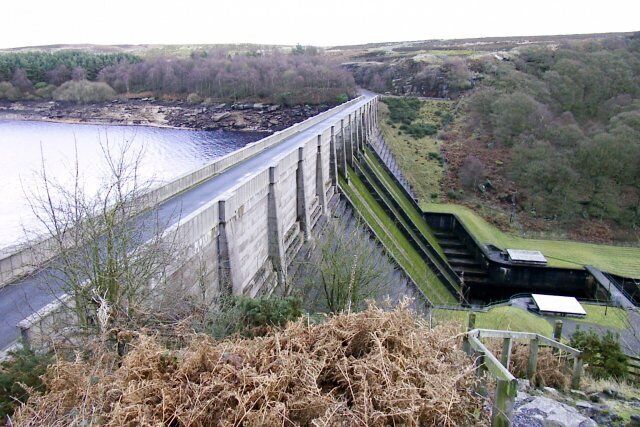 A large dam with a river flowing through it, surrounded by hills and sparse vegetation.