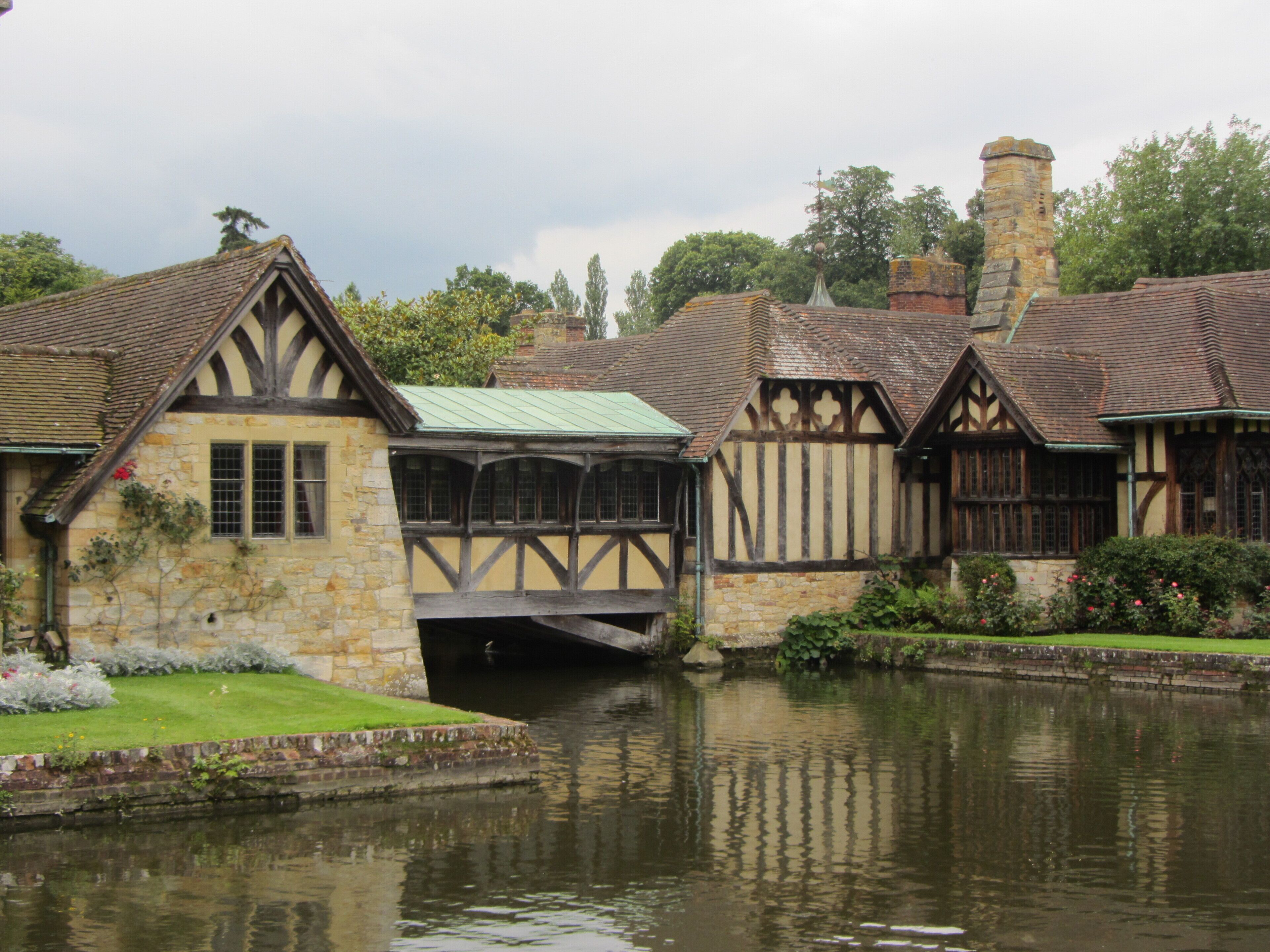 A traditional Tudor-style building with a stone facade and timber framing, adjacent to a calm river.