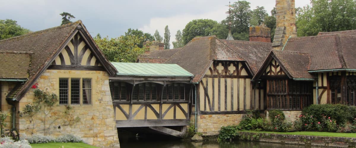A traditional Tudor-style building with a stone facade and timber framing, adjacent to a calm river.