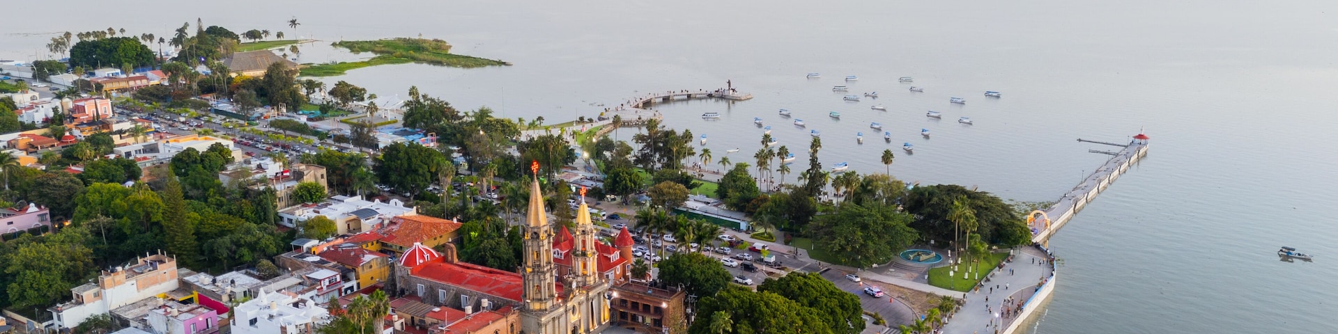 A coastal cityscape with a prominent church, a marina with boats, and a bridge connecting the land to the water.