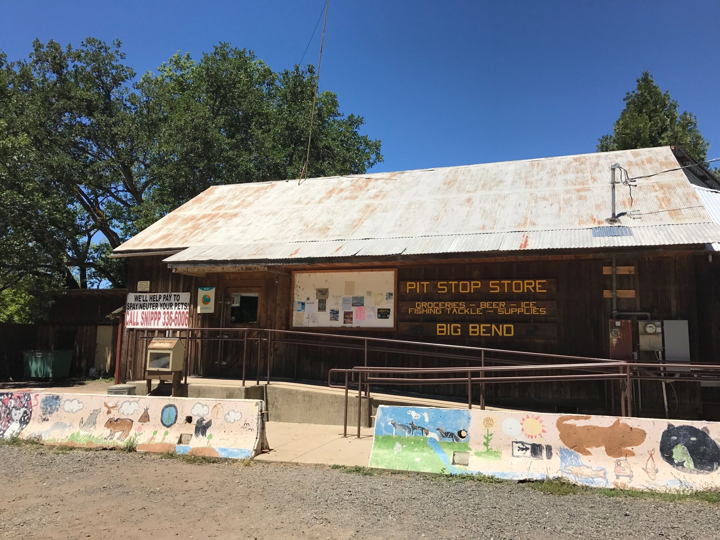 A rustic, weathered building with a sign advertising a pit stop store offering groceries, beer, ice, fishing tackle, and supplies.