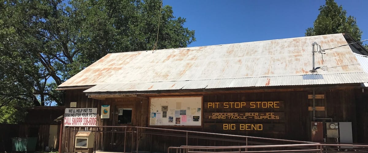 A rustic, weathered building with a sign advertising a pit stop store offering groceries, beer, ice, fishing tackle, and supplies.