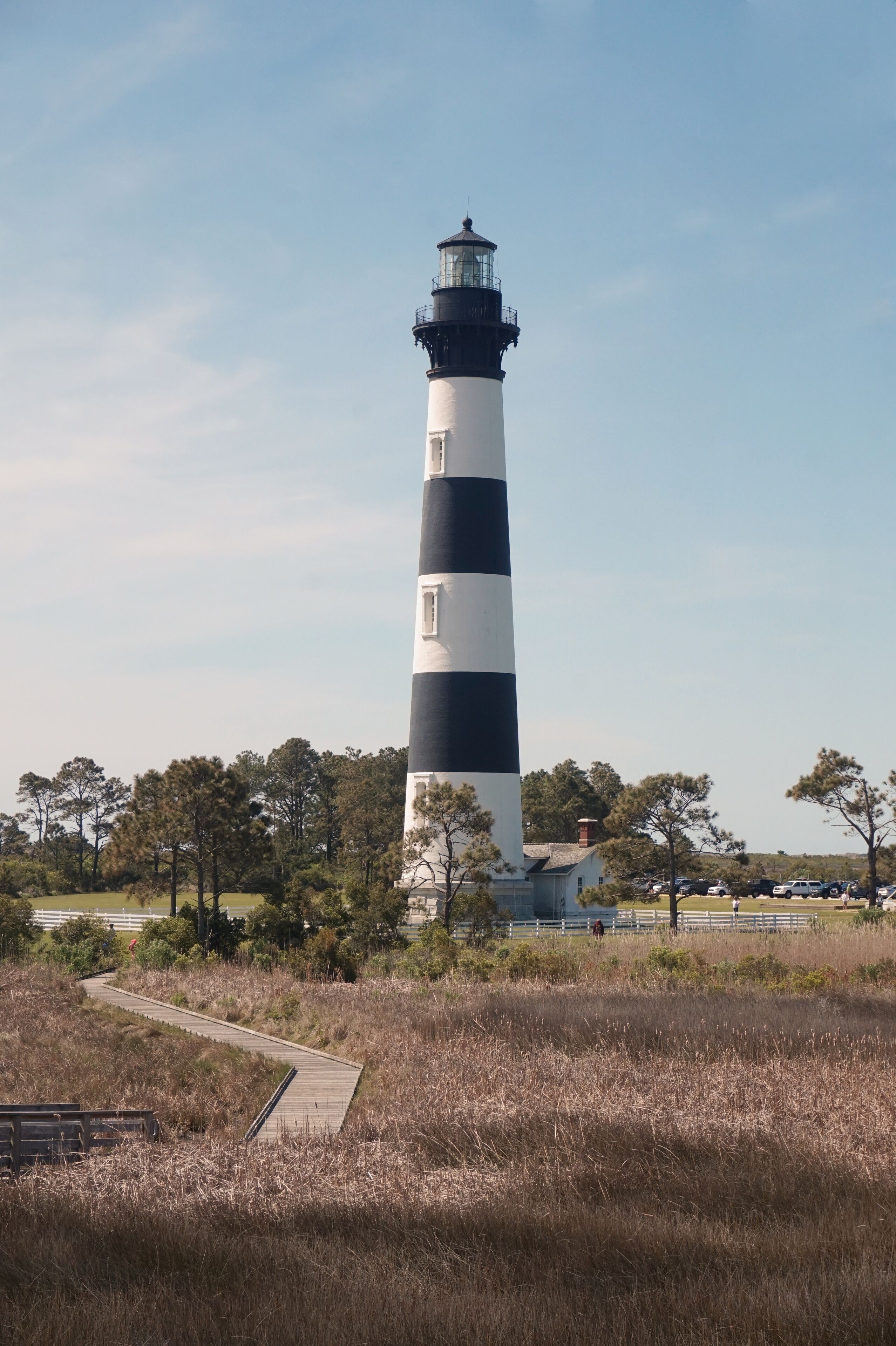A tall lighthouse with alternating black and white stripes, surrounded by trees and a boardwalk.