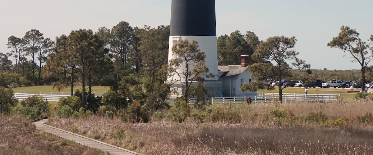 A tall lighthouse with alternating black and white stripes, surrounded by trees and a boardwalk.