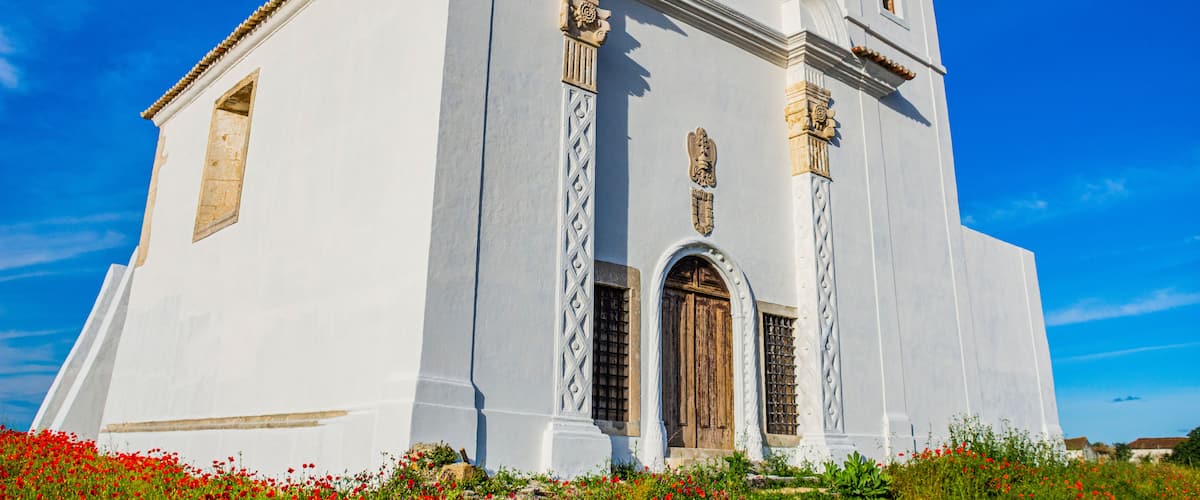A white church with a bell tower, arched windows, and a wooden door.