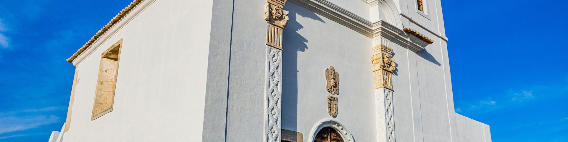 Une église blanche dotée d’un clocher, de fenêtres en arc de cercle et d’une porte en bois.