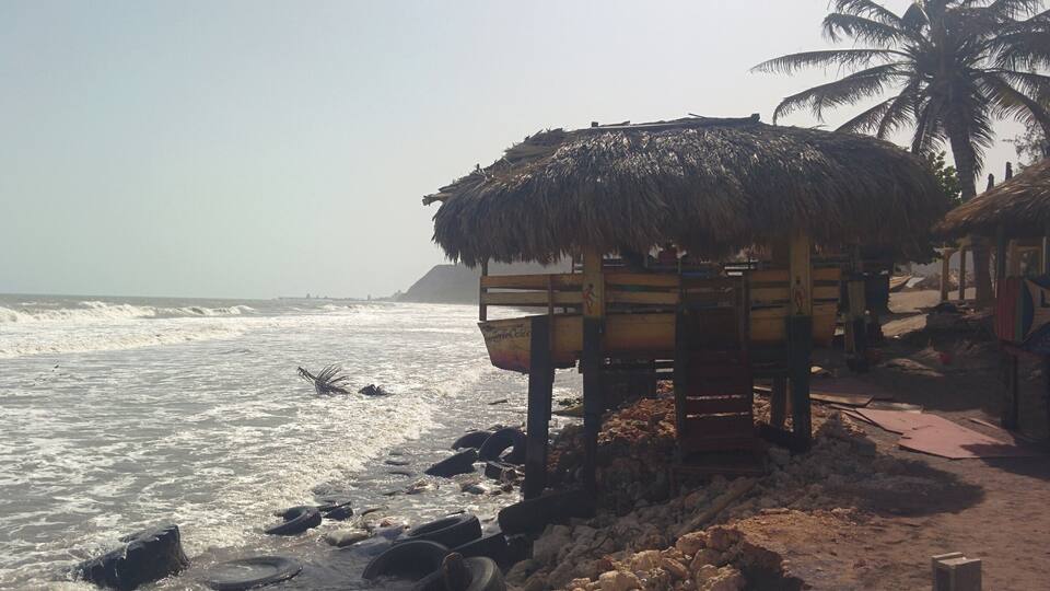 A beach with a thatched-roof hut, palm trees, and scattered tires on the shore.