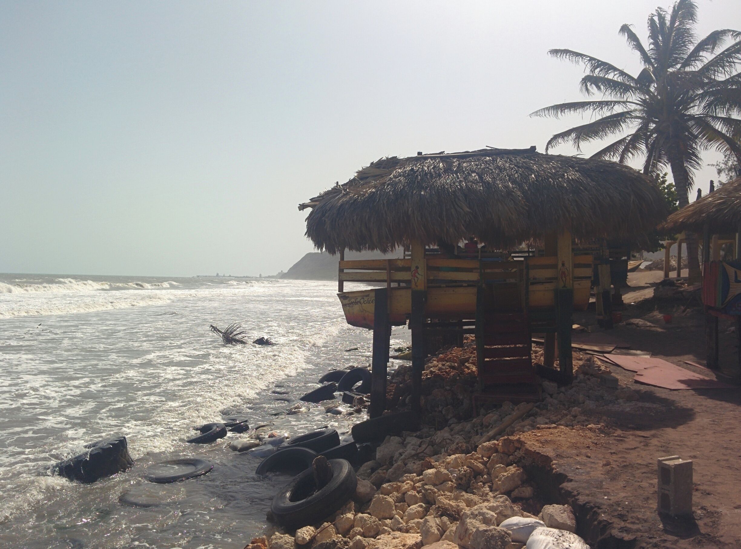 A beach with a thatched-roof hut, palm trees, and scattered tires on the shore.