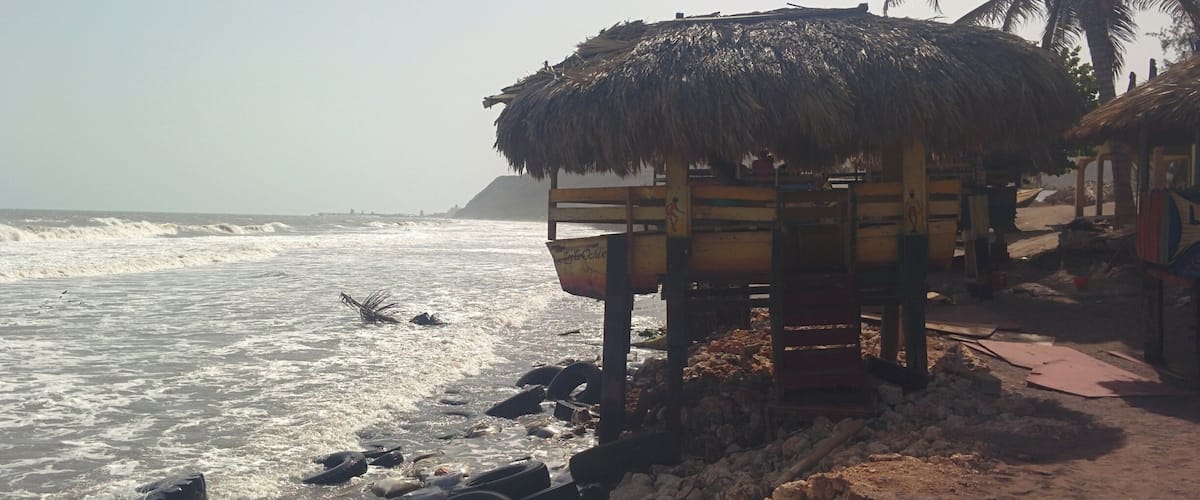 A beach with a thatched-roof hut, palm trees, and scattered tires on the shore.