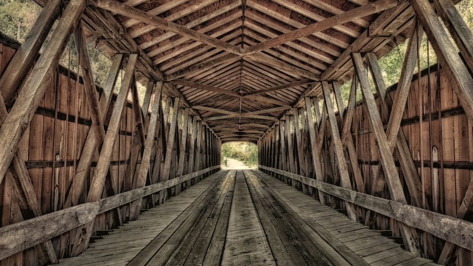 A wooden covered bridge with a symmetrical design and a central pathway.