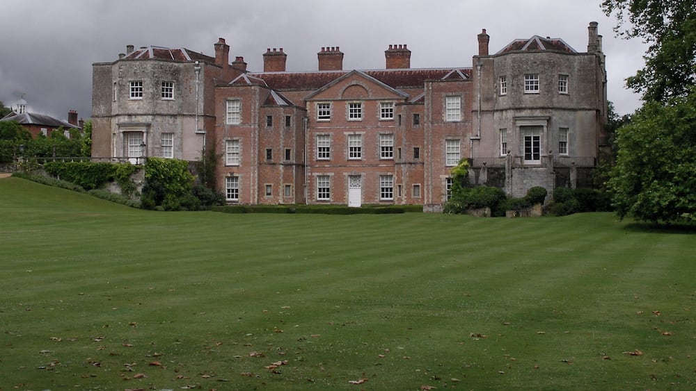 A large, historic building with a symmetrical facade, surrounded by a well-maintained lawn and mature trees.