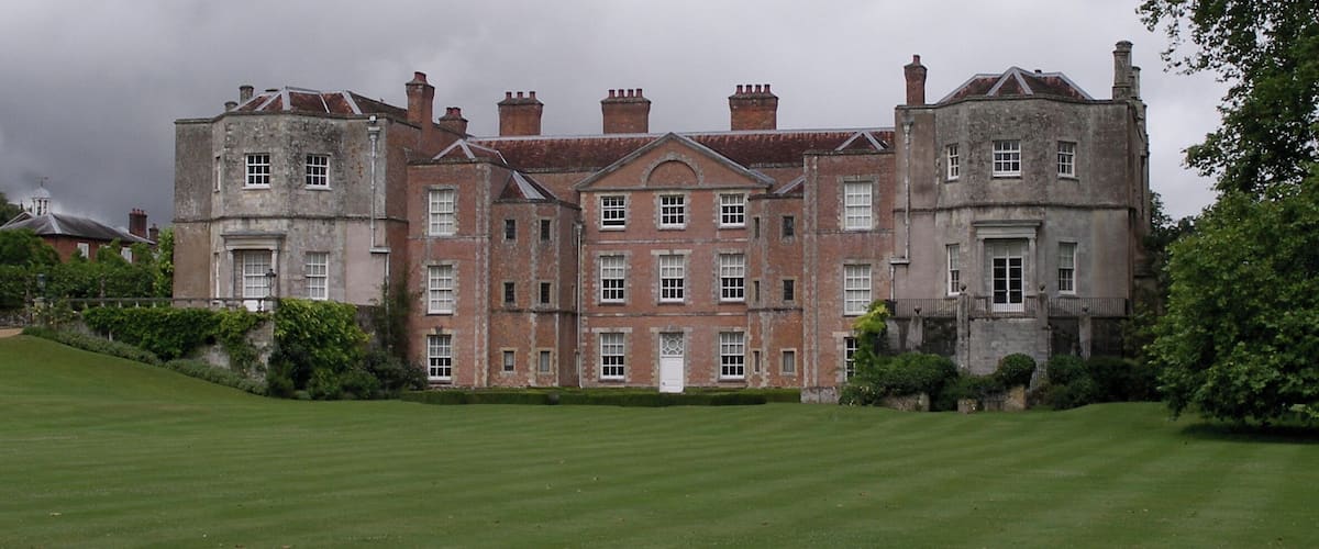 A large, historic building with a symmetrical facade, surrounded by a well-maintained lawn and mature trees.
