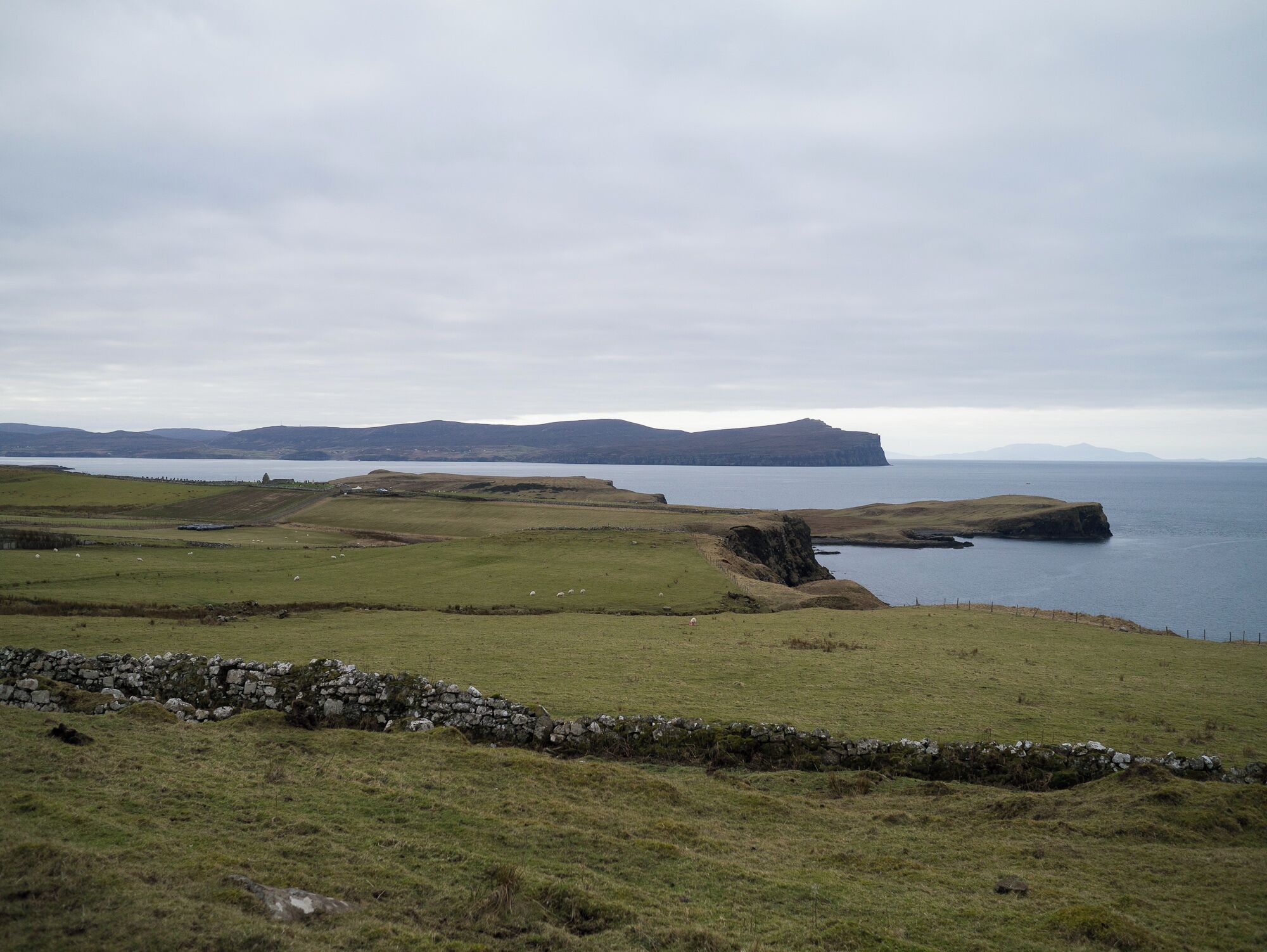 A coastal landscape with rolling hills, a stone wall, and a body of water.