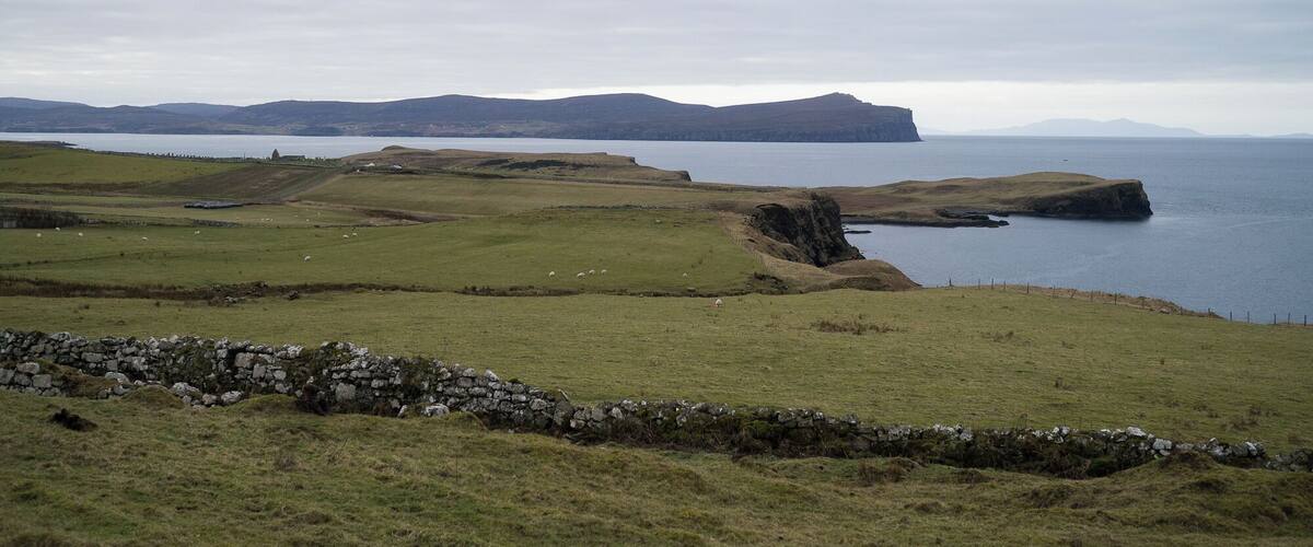 A coastal landscape with rolling hills, a stone wall, and a body of water.