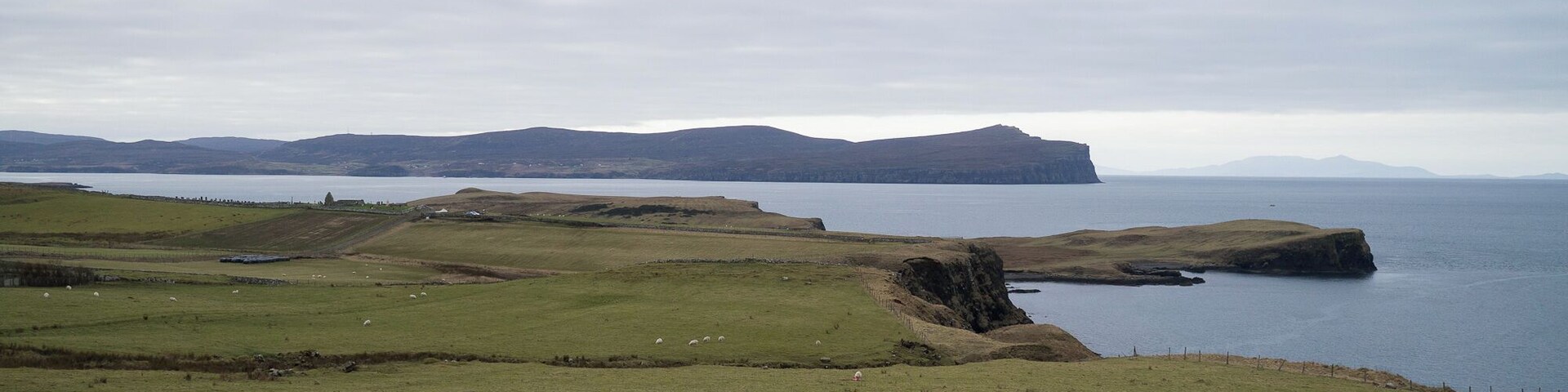 A coastal landscape with rolling hills, a stone wall, and a body of water.