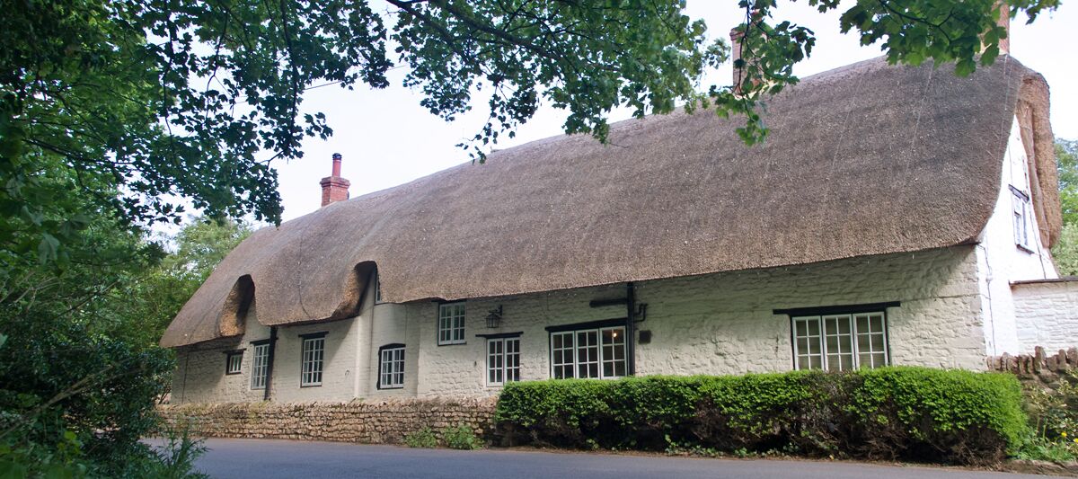 A traditional thatched-roof house with white walls and a stone foundation.