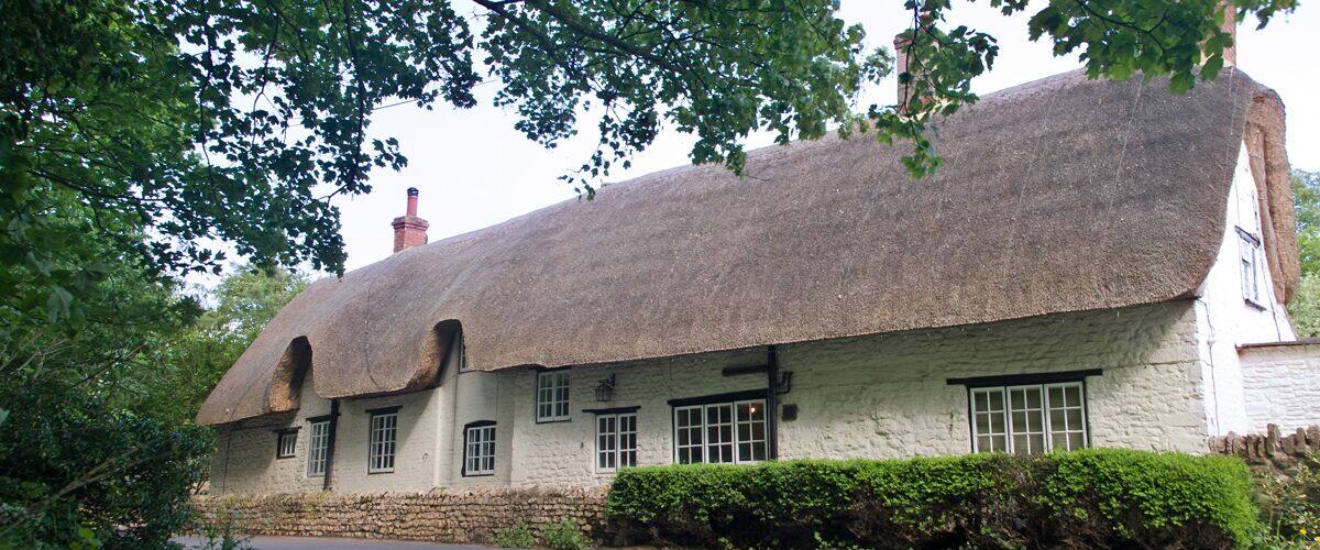 A traditional thatched-roof house with white walls and a stone foundation.