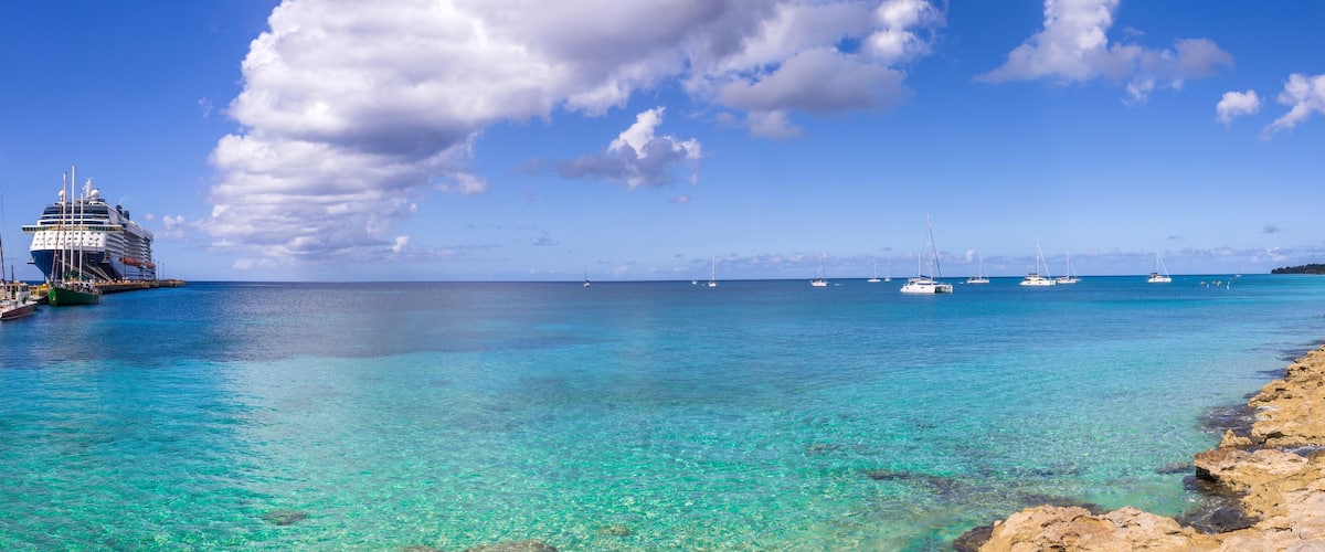 A cruise ship docked at a pier with clear turquoise water and a rocky shoreline.