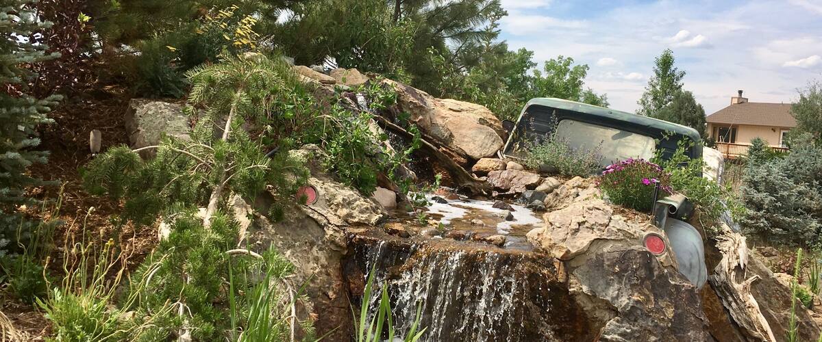 A rocky waterfall in a garden with a green vehicle parked nearby.