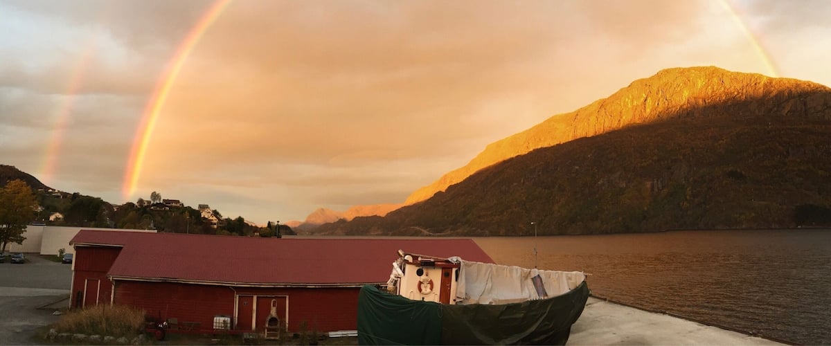 A rainbow over a lake with a mountain in the background and a red building in the foreground.