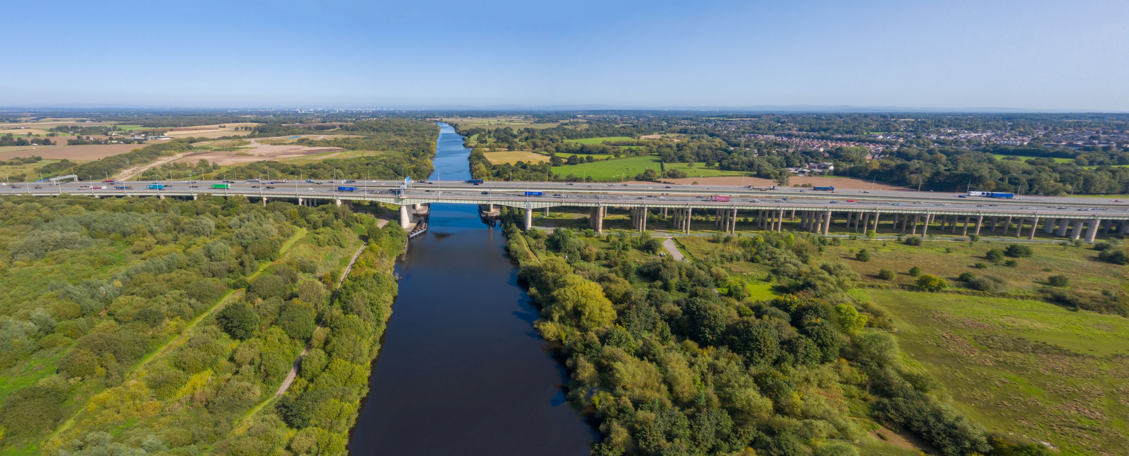A bridge over a river with surrounding greenery and a distant town.