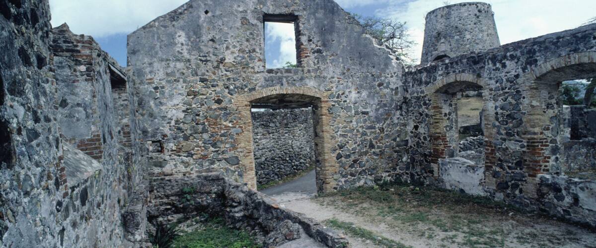 An old stone building with a central archway, surrounded by ruins and a small garden area.