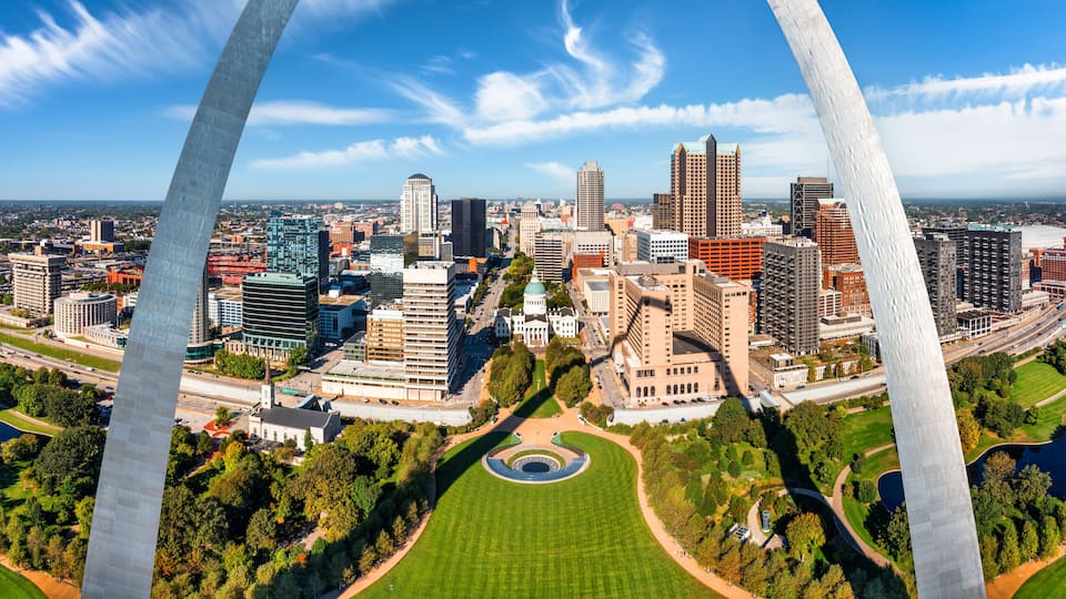 A cityscape with a prominent arch structure, a central green park, and various buildings including a large dome-shaped building.