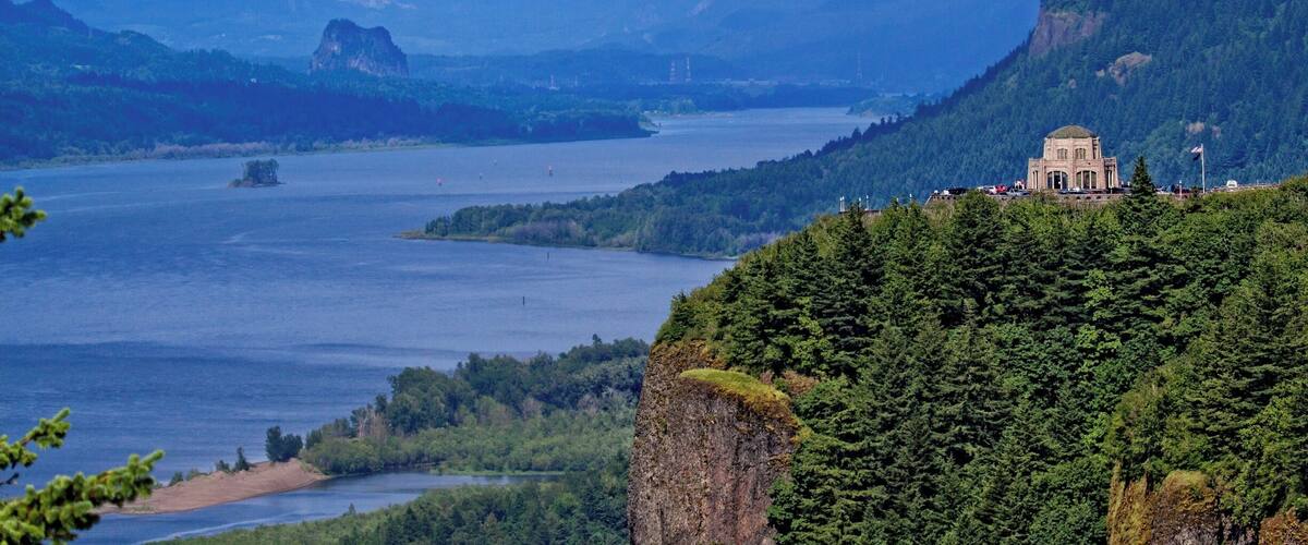 A lake surrounded by mountains, a building on a hill, and a forested area.