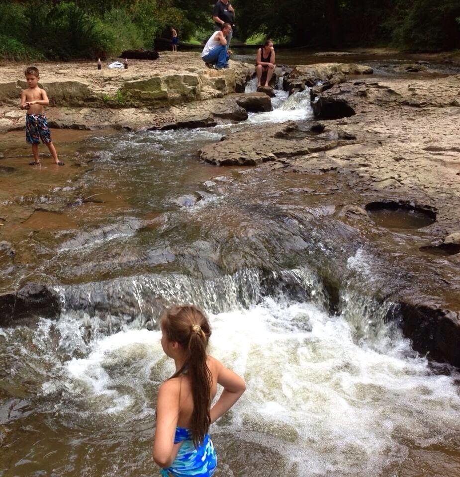 A rocky stream with people standing and sitting on the rocks.