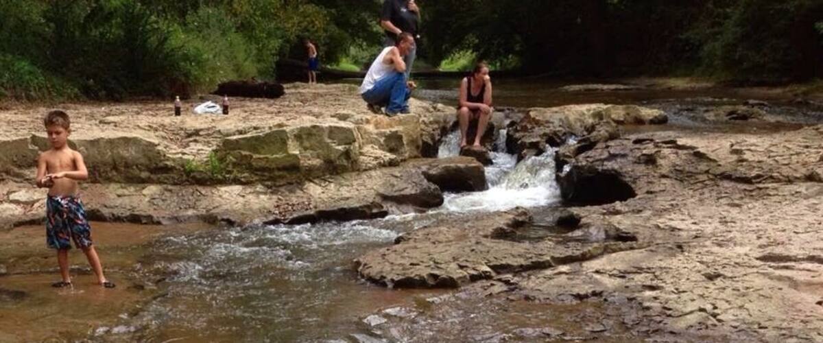 A rocky stream with people standing and sitting on the rocks.